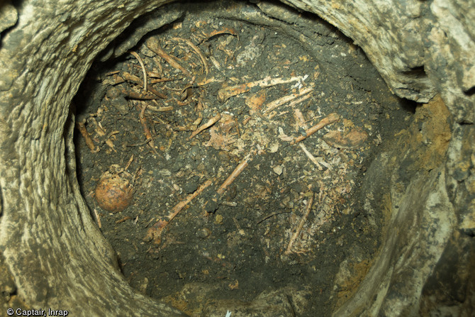 Vue générale d'un niveau de sépulture présentant, en haut légèrement à gauche, un individu en connexion partielle  assis  contre la paroi, VIIIe-Xe s., Entrains-sur-Noahain (Nièvre), 2013. Dans un puits antique de l'agglomération d'Intaranum, 20 à 30 corps ont été jetés simultanément, victimes d'un massacre ou d'une épidémie à dater entre les VIIIe et Xe s. 