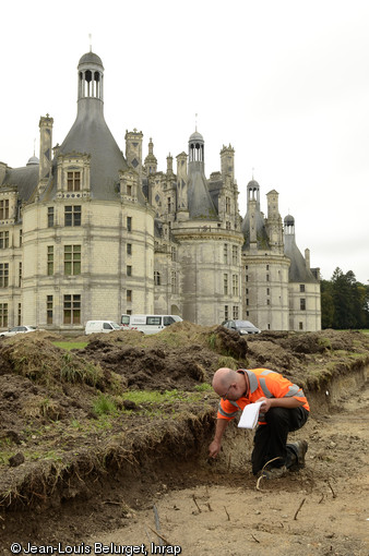 Fouille des vestiges visibles dans la coupe réalisée dans la partie orientale du site, château de Chambord (Loir-et-Cher), 2013. Les traces laissées par les jardins sont éphémères et difficiles à lire en surface dans le contexte d'un substrat composé de remblais hétérogènes. Leur identification nécessite l'observation fine des changements de sédiments. En arrière-plan, la tour de l'angle nord-est de l'enceinte du château.