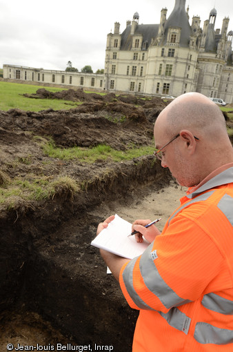 Enregistrement d'une des fosses de plantation du bosquet de marronniers qui occupait le carré nord-est du jardin anglais, château de Chambord (Loir-et-Cher), 2013.Les trous de plantation apparaissent comme des tâches sombres de 2,60 à 3 m de diamètre en surface. La fouille partielle permet d'observer la forme de la fosse d'origine et de son comblement, en partie effacés par le dessouchage de l'arbre.    