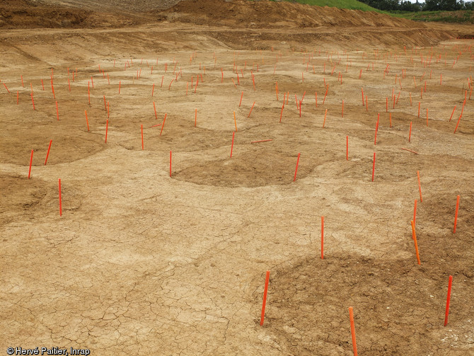 Vue générale de la mine des Rochardières à La Milesse (Sarthe), 2012.Les vestiges d’une ancienne mine de fer y ont été fouillés de mars 2011 à début 2012. Le site a été terrassé jusqu’à 4 mètres de profondeur et plusieurs centaines de fosses et de puits d’extraction de minerai ont été dégagés. Les archéologues matérialisent les zones d’extraction en les entourant de piquets orange.