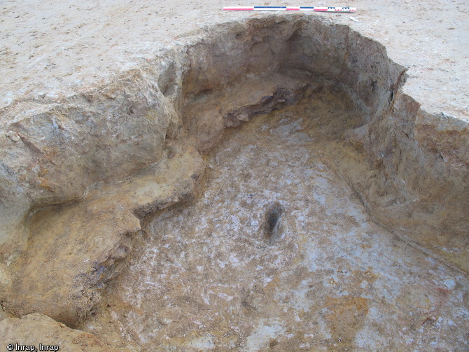 Extrémité d'une galerie dans laquelle a été extrait du minerai de fer, La Milesse (Sarthe), 2012.On devine la présence de minerai grâce à la couche festonnée conservée sur le bord gauche. Le creusement dans le sol au centre du boyau pourrait correspondre à l'appui d'un étai servant à soutenir le plafond.