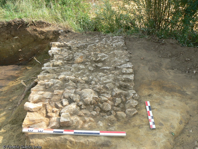 Empierrement soutenant une passerelle en bois qui permettait de franchir l'enclos entourant un &eacute;tablissement agricole m&eacute;di&eacute;val des XIIIe-XIVe&nbsp;s. &agrave; La Chapelle (Sarthe), 2011.La localisation du site, aux marges de plusieurs territoires paroissiaux, laisse &agrave; penser qu'il pourrait s'agir d'un &eacute;tablissement  pionnier , destin&eacute; &agrave; la mise en valeur de terres agricoles.