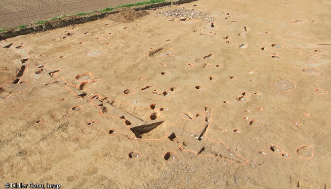 Vue d'un secteur de la fouille menée à Vassé, Torcé (Ille-et-Vilaine), 2012. Au premier plan, on observe un fossé moderne, puis une concentration de structures des VIIe-IXe s. (trous de poteaux, silos enterrés, structures de combustion). Au fond, la zone empierrée est un chemin moderne lié au manoir voisin construit au XVIe s.