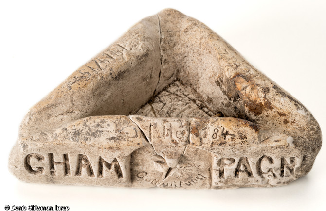 Artisanat de tranchée : cendrier triangulaire taillé dans un bloc de craie, avec plusieurs inscriptions. Au premier plan :  Champagne  la localisation du Front, au-dessous de la Croix de fer  Gott mit Uns  (Dieu avec nous), au-dessus  I.Reg (1)84  (nom du régiment). A droite et à gauche :  1914/15-1916  et  (P)E(T)UZU...  (Peut-être le nom du soldat). Découvert dans une latrine d'un terrain d'aviation allemand datant de la Grande Guerre à Warmeriville (Marne), 1913. 