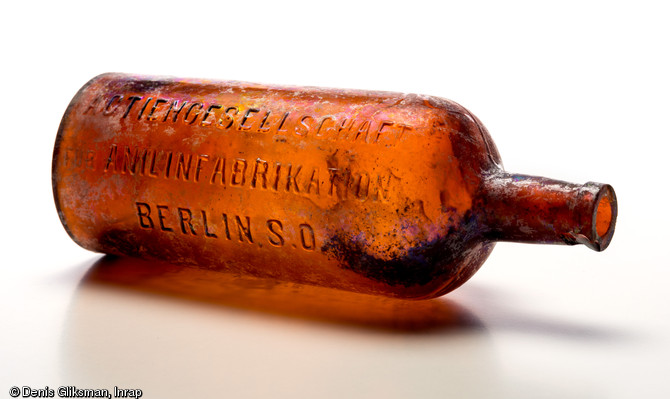 Bouteille en verre d'aniline avec inscription  Actiengesellschaft für Anilinfabrikation Berlin S.O.  (Société de fabrication d'aniline, Berlin), l'aniline est un composé organique aromatique de formule chimique utilisé pour la teinture des tissus. Découverte dans une latrine d'un terrain d'aviation allemand datant de la Grande Guerre à Warmeriville (Marne), 2013.