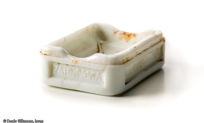 Boîte en porcelaine de dentifrice de la marque Bergmann à Waldheim (Saxe), avec plusieurs inscriptions sur les flancs :  A.H.A. Bergmann-Waldheim SA-Bergmanns-Zahnpasta  et sur le dessous  Bergmann-Waldheim-1/Sachsen. Découverte dans une latrine d'un terrain d'aviation allemand datant de la Grande Guerre à Warmeriville (Marne), 2013.