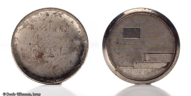 Montre &agrave; gousset en alliage cuivreux, d. 5cm,&nbsp; dont l'ext&eacute;rieur est d&eacute;cor&eacute; avec des motifs de style Art d&eacute;co avec un emplacement d&eacute;di&eacute; aux initiales  JB . L'int&eacute;rieur du bo&icirc;tier porte l'inscription  Russland/1941-1943/Gfr Baldo/Frankreich/1943  grav&eacute;e par son propri&eacute;taire J. Baldo, caporal (gefreiter) allemand, qui relate son parcours militaire de la campagne de Russie &agrave; la France. Datant de la Bataille de Normandie (&eacute;t&eacute; 1944) et d&eacute;couverte dans le comblement d'un trou de bombe dans le ch&acirc;teau de Caen (Calvados), 2011.