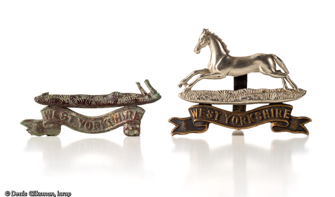 Insigne de coiffure incomplet (&agrave; gauche) du  West Yorkshire Regiment  (Prince of Wale's Own), unit&eacute; d'infanterie r&eacute;guli&egrave;re de l'arm&eacute;e de terre britannique. Datant de la Bataille de Normandie (&eacute;t&eacute; 1944) et d&eacute;couvert &agrave; Epron (Calvados), 2011.  Si aucune unit&eacute; de ce r&eacute;giment n'est pr&eacute;sente officiellement en Normandie, quelques soldats ont certainement &eacute;t&eacute; envoy&eacute;s en soutien d'infanterie, afin de combler les pertes dues aux combats ou d&eacute;tach&eacute;es &agrave; un &eacute;tat-major. Ces soldats ont tout naturellement continu&eacute; &agrave; porter leur insigne d'origine.  L'insigne complet (&agrave; droite) porte sur la banderolle
