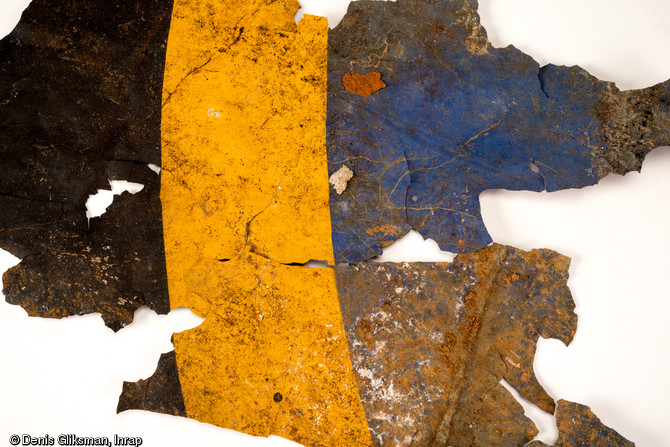 Fragments d'une cocarde britannique (compos&eacute;e de l'ext&eacute;rieur vers l'int&eacute;rieur de bleu, blanc, rouge et cercl&eacute;e de jaune) qui se situait sur le fuselage d'un planeur Horsa. Elle diff&egrave;re de celles des ailes par la pr&eacute;sence du liser&eacute; jaune. Datant du jour J de la Bataille de Normandie (nuit du 5 au 6 juin 1944) et d&eacute;couverts dans un trou d'homme &agrave; Ranville (Calvados), 2009.