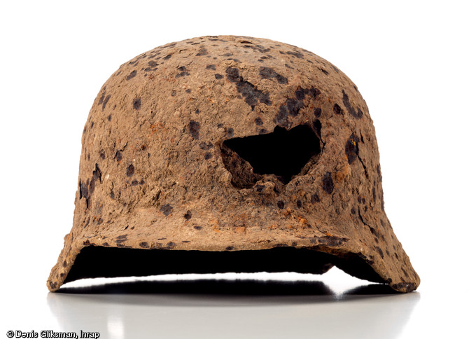 Casque en acier allemand (Stahlhem), mod&egrave;le 1935, d. 25 cm et h. 25 cm, perfor&eacute; de trois impacts probablement dus &agrave; des &eacute;clats d'obus, dont un frontal plus important. Datant de la Bataille de Normandie et d&eacute;couvert dans une fosse &agrave; Soumont-Saint-Quentin (Calvados), 2008. 