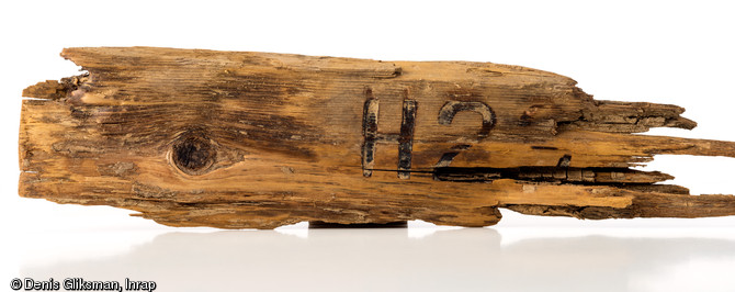 Fragment du dessus d'un couvercle de munitions en bois (L. 25 cm), d'origine allemande, sur lequel est indiqu&eacute;, avec un marquage &agrave; chaud, le calibre et le type de pi&egrave;ce d'artillerie employ&eacute;e ;  H  pour  Haubitze  (obusier)&nbsp; 2(3 ou 9?). La ville de Tilly-sur-Seulles, fut le th&eacute;&acirc;tre de violents combats, pendant l'op&eacute;ration Perch men&eacute;e du 7 au 15 juin 1944 par les troupes du XXXe Corps britannique contre la  Panzer Lehr Division  allemande. D&eacute;couvert dans une fosse &agrave; Tilly-sur-Seulles (Calvados), 2014.