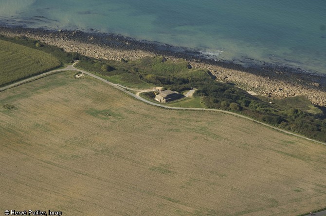 Vue aérienne de la batterie de Longues-sur-Mer (Calvados), 2011. Construite à partir de novembre 1943 par l’armée allemande, au bord d’une falaise à 65 mètres d’altitude. L’une des mieux conservées parmi la trentaine de batteries côtières de la région et possède encore 2 de ses 4 pièces d’artillerie d’origine tchèque (Skoda, calibre 150 mm).  Elle fut neutralisée dès le 6 juin 1944 par les tirs du croiseur de la Royal Navy HMS Ajax ainsi que les croiseurs français Georges-Leygues et Montcalm. Immortalisée dans le film « Le Jour le plus long ». 