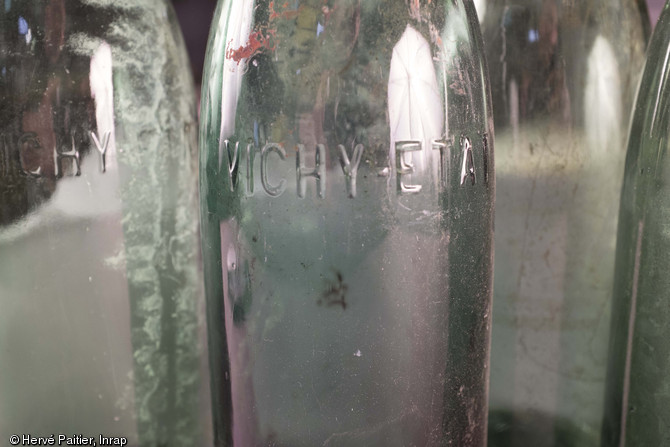 Bouteilles d'eau de Vichy provenant des b&acirc;timents de la Kommandatur, d&eacute;couvertes dans une fosse d&eacute;potoir autour de la cath&eacute;drale &agrave; S&eacute;es (Orne), 2013.  La mention  Etat  est due &agrave; la gestion sous concession de l'Etat depuis 1853, et n'a aucun rapport avec la d&eacute;signation  Etat fran&ccedil;ais  du R&eacute;gime de Vichy pendant l'occupation. 