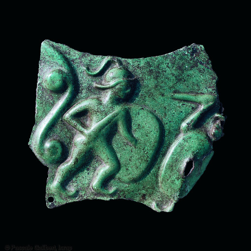 Fragment de t&ocirc;le de bronze perfor&eacute;e figurant deux guerriers celtes au combat.
