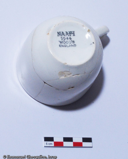 Tasse à thé en faïence, datée de 1944, de fabrication anglaise pour l'institution du N.A.A.F.I. (Navy, Army and Air Force Institute). Cette institution, créée en 1921 par le gouvernement britannique apportait aux soldats, loisirs et nourriture. Les effectifs du N.A.A.F.I. comprenaient plus de 7.000 cantines ou points de vente et employaient plus de 96.000 personnes en avril 1944, de par le monde. Découverte dans une fosse près du camp de prisonniers allemands sur le site de Fleury-sur-Orne (Calvados).