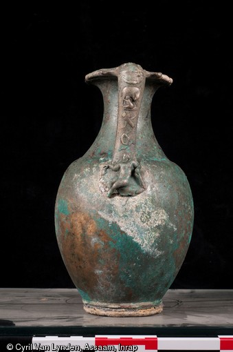 Pot en alliage cuivreux comportant une anse orn&eacute;e d'une sc&egrave;ne mythologique, repr&eacute;sentant sur la partie inf&eacute;rieure, Hercule se reposant sur sa massue et sur la partie sup&eacute;rieure, son fils T&eacute;l&egrave;phe accompagn&eacute; d'une biche. Pi&egrave;ce d'un service &agrave; vin du IIIe si&egrave;cle de notre &egrave;re, d&eacute;couvert sur le site d'Argentomagus &agrave; Saint-Marcel (Indre), 2013.