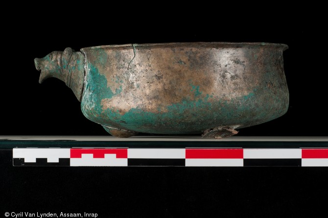 Bassin en alliage cuivreux, muni d'un filtre et d'un bec verseur orn&eacute; d'une t&ecirc;te zoomorphe, repr&eacute;sentant probablement un porc. Il repose sur trois pieds r&eacute;alis&eacute;s par des cabochons en t&ocirc;le scell&eacute;s au plomb. Pi&egrave;ce d'un service &agrave; vin du IIIe si&egrave;cle de notre &egrave;re, d&eacute;couvert sur le site d'Argentomagus &agrave; Saint-Marcel (Indre), 2013.