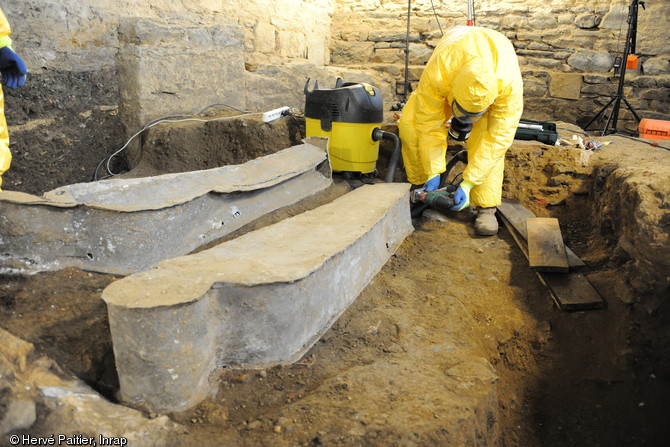 Dégagement d'un cercueil en plomb découvert au couvent des Jacobins, Rennes (Ille-et-Vilaine), 2015.  Les cercueils en plombs sont ouverts à la scie sauteuse et les archéologues travaillent avec des combinaisons étanches pour se protéger des particules de métaux lourds, de possibles gaz de décomposition et des champignons potentiellement présents dans ces milieux confinés. 